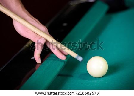 Billiards. Billiard balls on green table and white ball on the foreground. Hand of someone who is playing pool.
