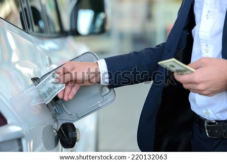 Hand of businessman that puts money into the tank of his car instead of gasoline at filling stations. Concept of expensive fuel