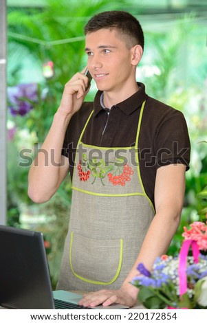 Florist man working with flowers at a greenhouse. talking on the phone.