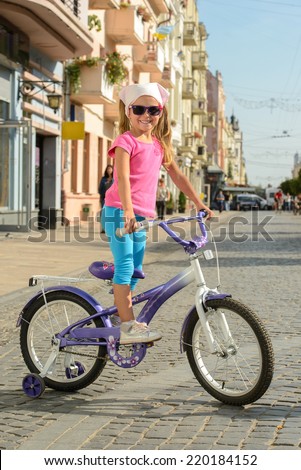 Beautiful smiling little girl riding a bike on the street in city