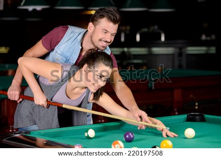 Young couple plays billiards in the dark billiard club