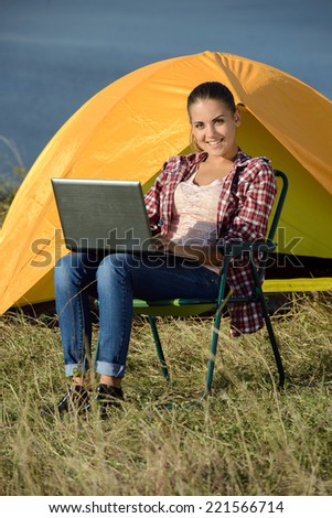Portrait of succesful woman with laptop sitting in folding chair near camp tent outdoors