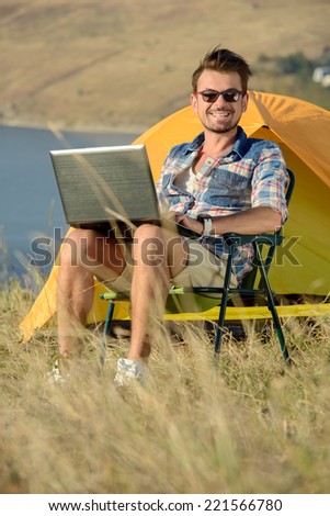 Portrait of succesful man with laptop sitting in folding chair near camp tent outdoors