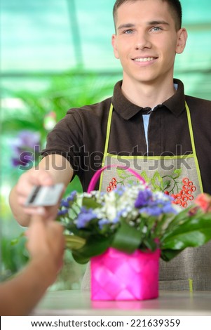 Young man working as florist giving credit card to customer after purchase.