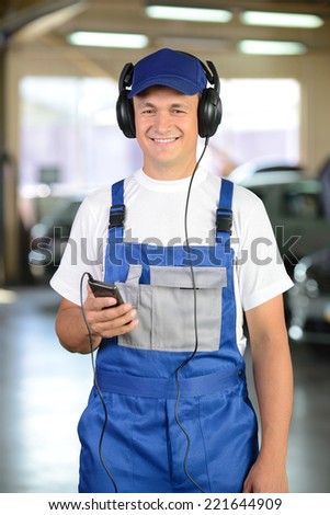 Portrait of auto mechanic, listening to music in headphones. Car background