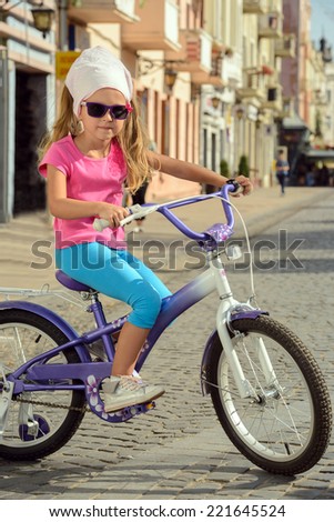 Beautiful smiling little girl riding a bike on the street in city