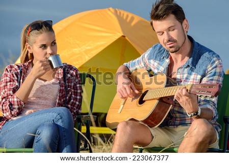 Cute man serenading his girlfriend on camping trip on a sunny day