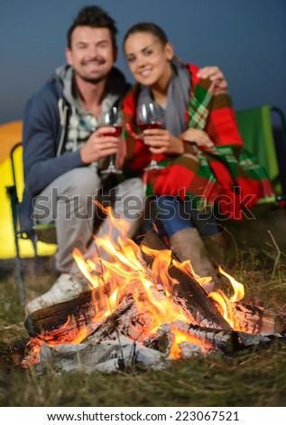 Romantic evening. Charming couple near a fire while camping drinking wine