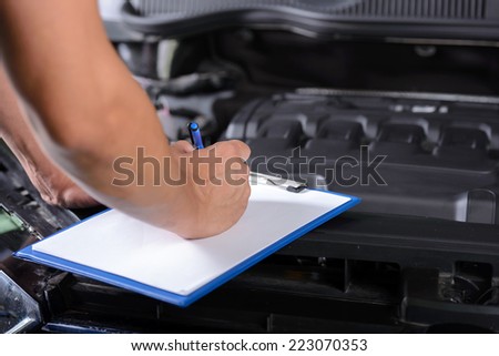 Mechanic in auto repair shop standing next to car with open hood