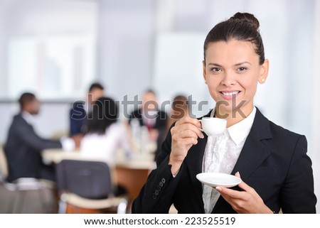 Business woman, drinking tea or coffee, people group in background at modern bright office indoors