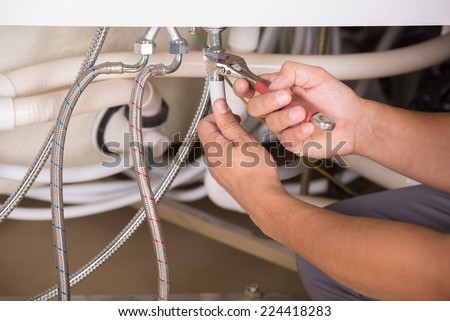 Hands repairing the plumbing pipes of an electric boiler with a spanner. Close-up.