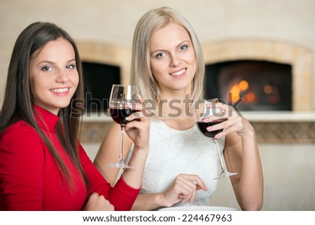 Young women in restaurant cheering with red wine.