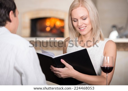 Young couple in restaurant cheering with red wine. The woman are looking at the menu-card.