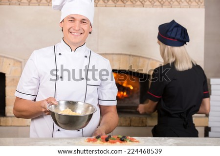 Two chefs are in white and black uniform at the work in a pizzeria.