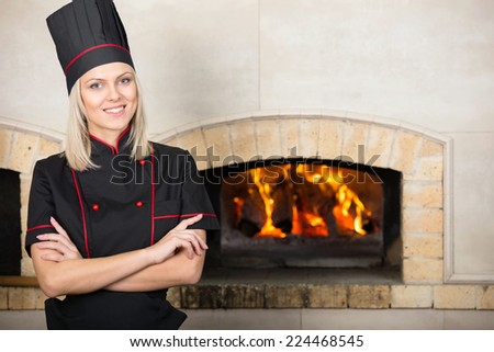 Handsome woman, chef baker in black uniform, the background of the oven.