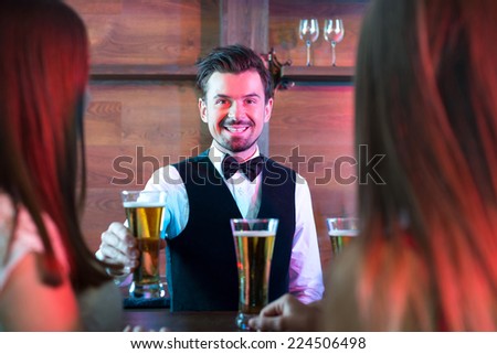 Freshly tapped beer. Handsome smiley bartender stretching out beer mugs and smiling