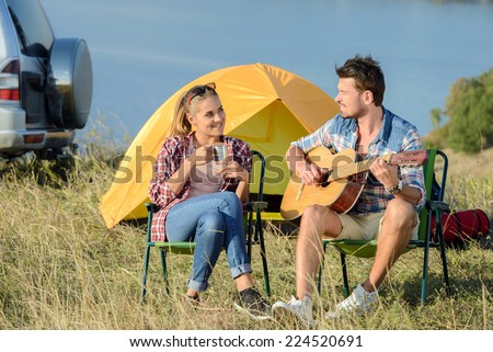 Cute man serenading his girlfriend on camping trip on a sunny day