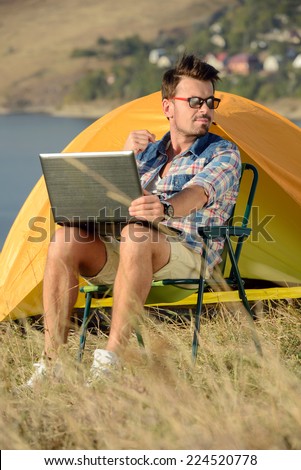 Portrait of succesful man with laptop sitting in folding chair near camp tent outdoors