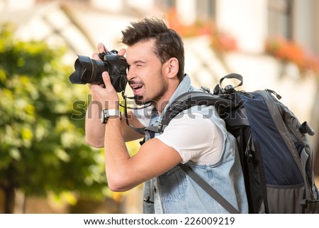 Portrait of happy young man, tourists with camera in the city.