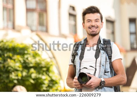 Portrait of happy young man, tourists with camera in the city.