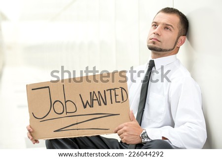 Unemployed young man is sitting with a sign Job wanted.