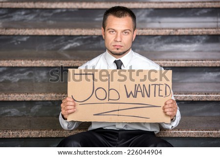 Young businessman is holding sign Wanted job, sitting on the stairs.