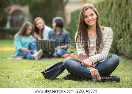 Portrait of a smiling college girl with blurred students are sitting in the park.