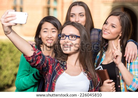Portrait of female students that are making pictures with university building in the background.