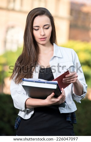 Portrait of a young beautiful student with university building in the background. She is holding books in hands.