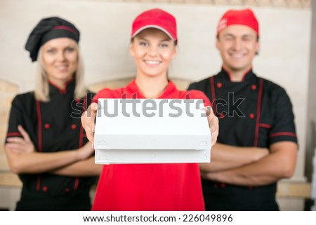 Delivery woman with boxes of pizza and two happy chef in black uniform.