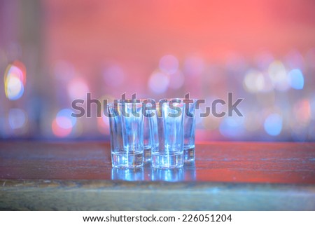 Four shots of tequila on a wooden table bar on the background of bright lights of the bar