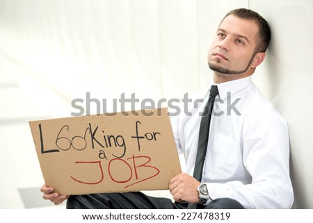 Unemployment. Young businessman is squatting with sign Looking for a job, outdoors.