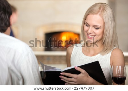 Young couple in restaurant cheering with red wine. The woman are looking at the menu-card and smiling.