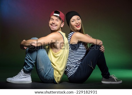 A couple of young dancers man and woman on the colored, foggy background is sitting back together on the floor.