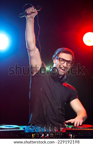 Portrait of a young DJ at work with a microphone and the club lights on the background.