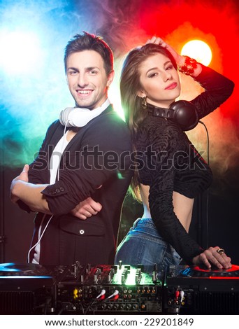 Portrait of two DJs with mixer in the club. Light and fog on the background.