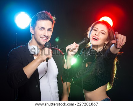Portrait of two happy DJs with microphones in the club on a background of light.