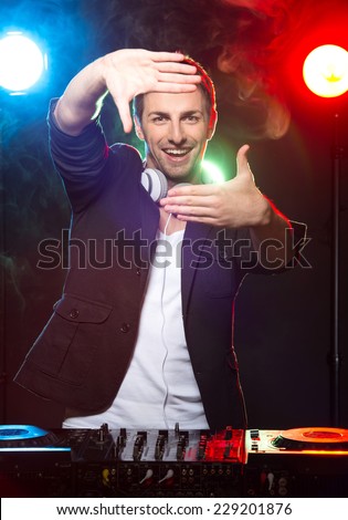 Portrait of a young smiling dj with mixer, on foggy background.