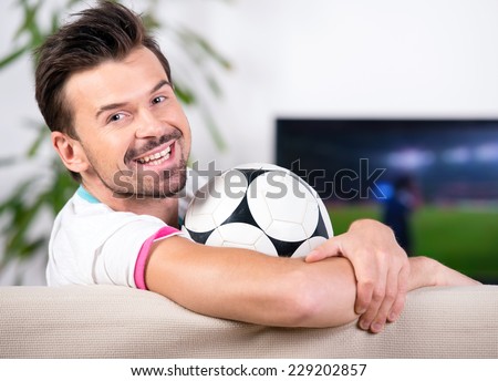 Smiling young man with soccer ball while watching the game. Looking at the camera.