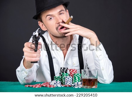 Wealthy man is playing poker in casino. With hat, gun, cigar and a glass of whiskey.