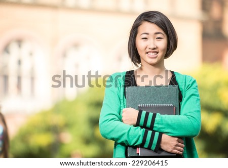 Portrait of a young beautiful asian student with university building in the background.