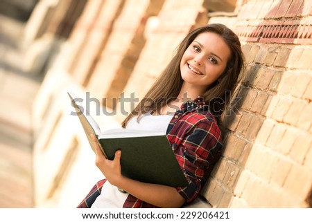 Portrait of a young smiling female student with book. The university building in the background.