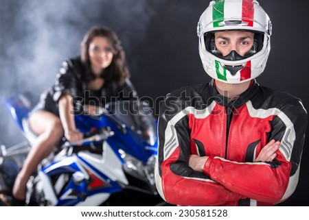 Portrait of motorcyclist and an attractive woman is posing on motorcycle. Foggy black background.