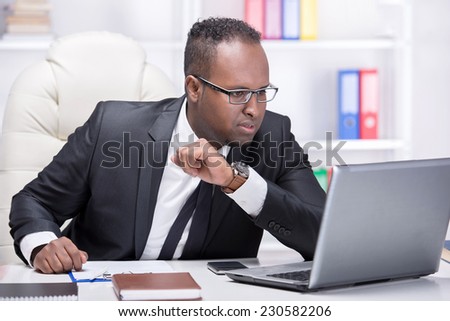 Businessman with laptop. Young African businessman is looking at laptop in his office.