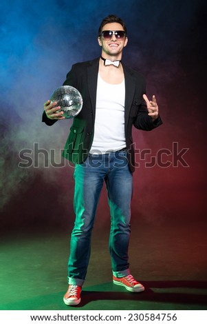 Portrait of young handsome man with mirror ball on a color background and fog.