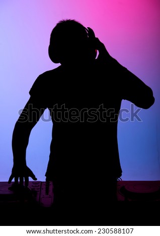 DJ at work. Young man is spinning on turntable while isolated on colored background.