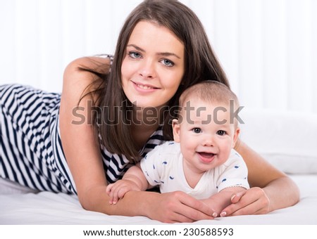 Lovely mother with her little baby boy are  laying in bed and looking at the camera.