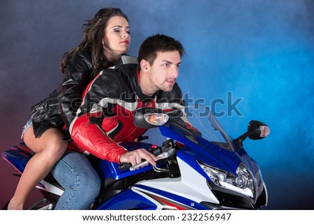 Young beautiful couple on a motorcycle. On a colored and foggy background.