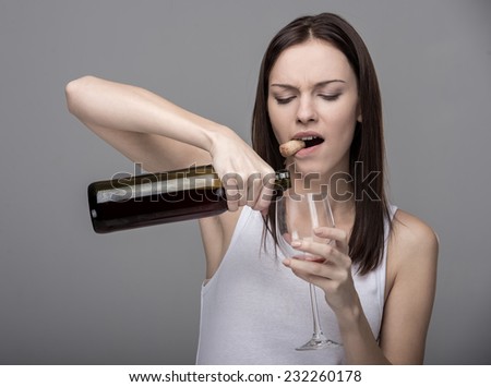 Young woman pours wine into a glass. Concept of bad habits.