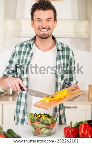 Smiling man is cooking vegetable salad in the kitchen.